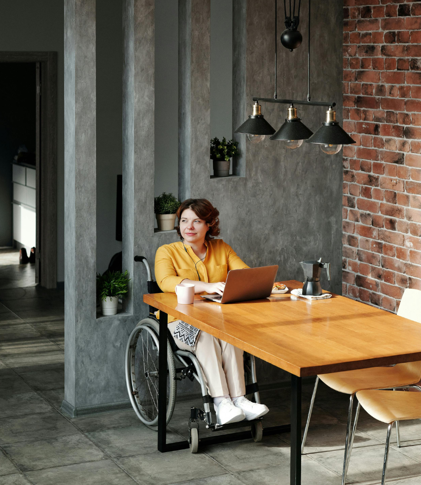 woman in a wheelchair sitting in an office space using her laptop while smiling